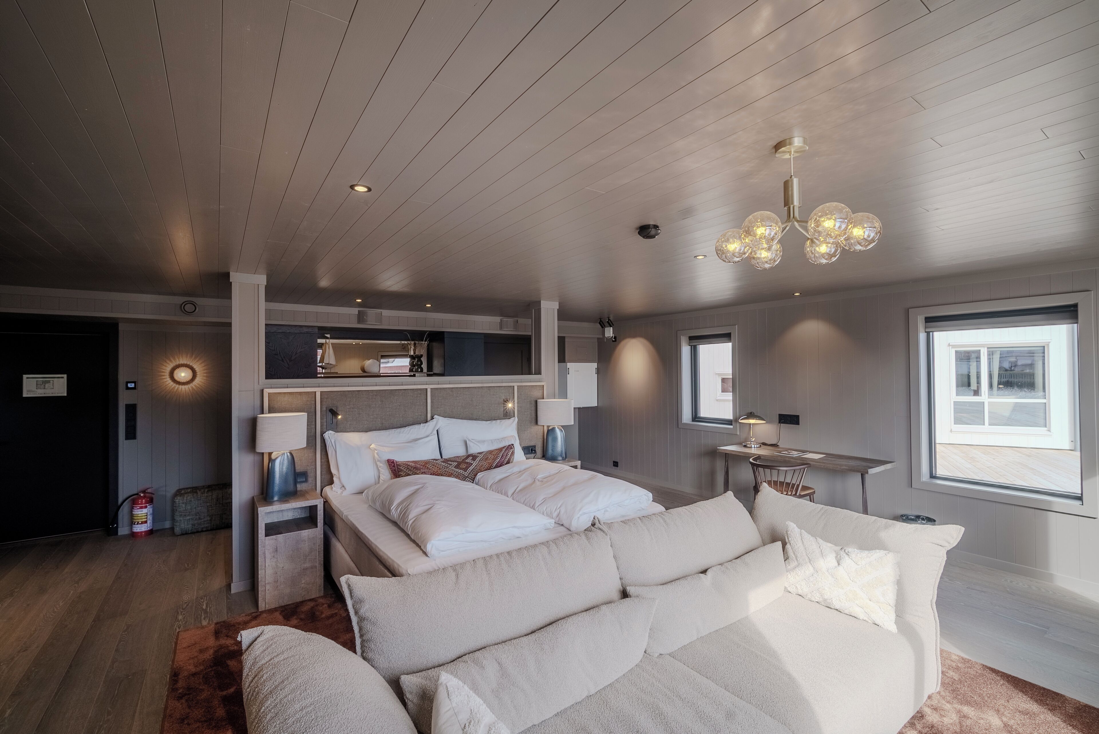 A modern bedroom with a large bed, bedside tables, a desk, and a window.