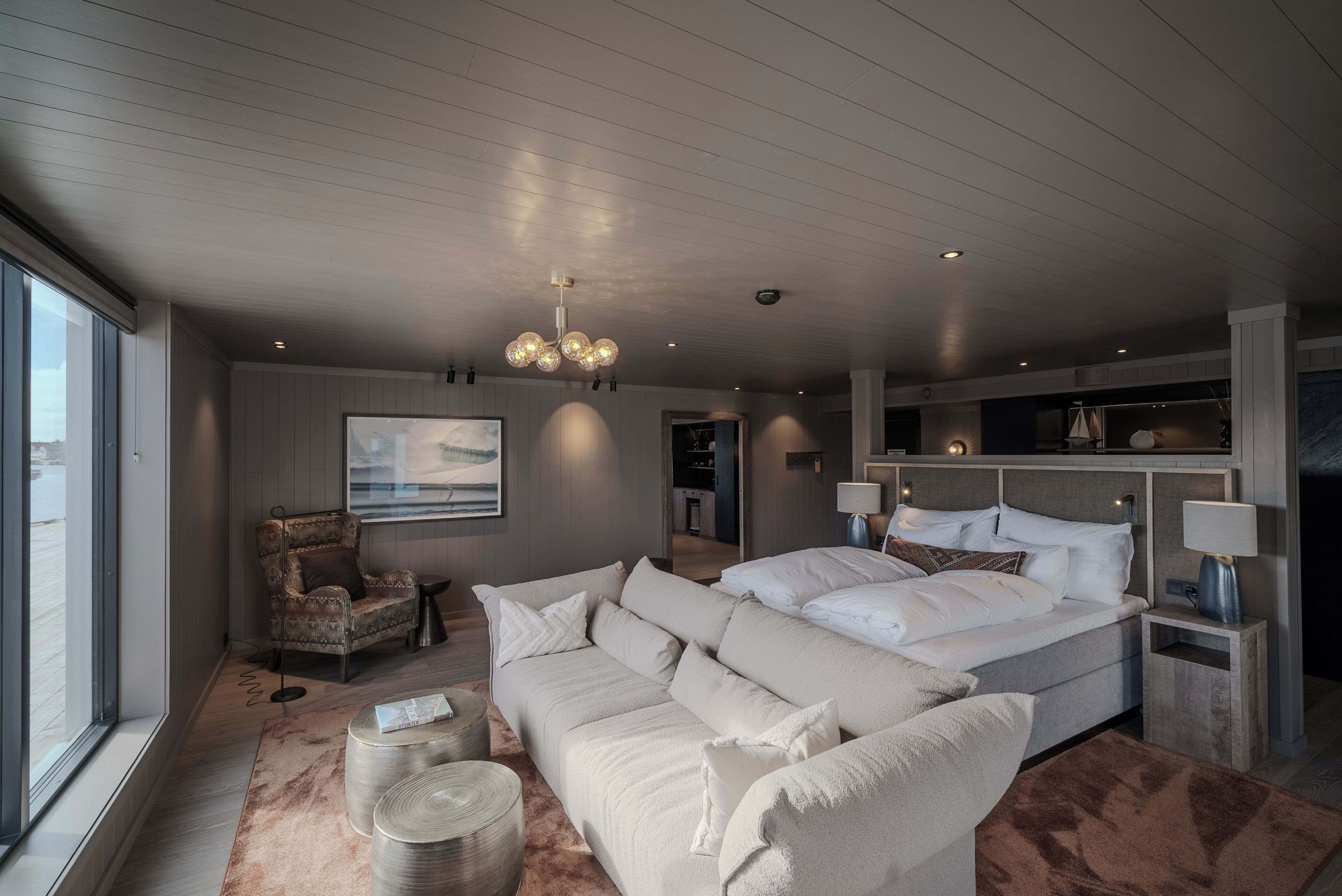 A modern bedroom with a large bed, a sofa, a chair, and a small table.