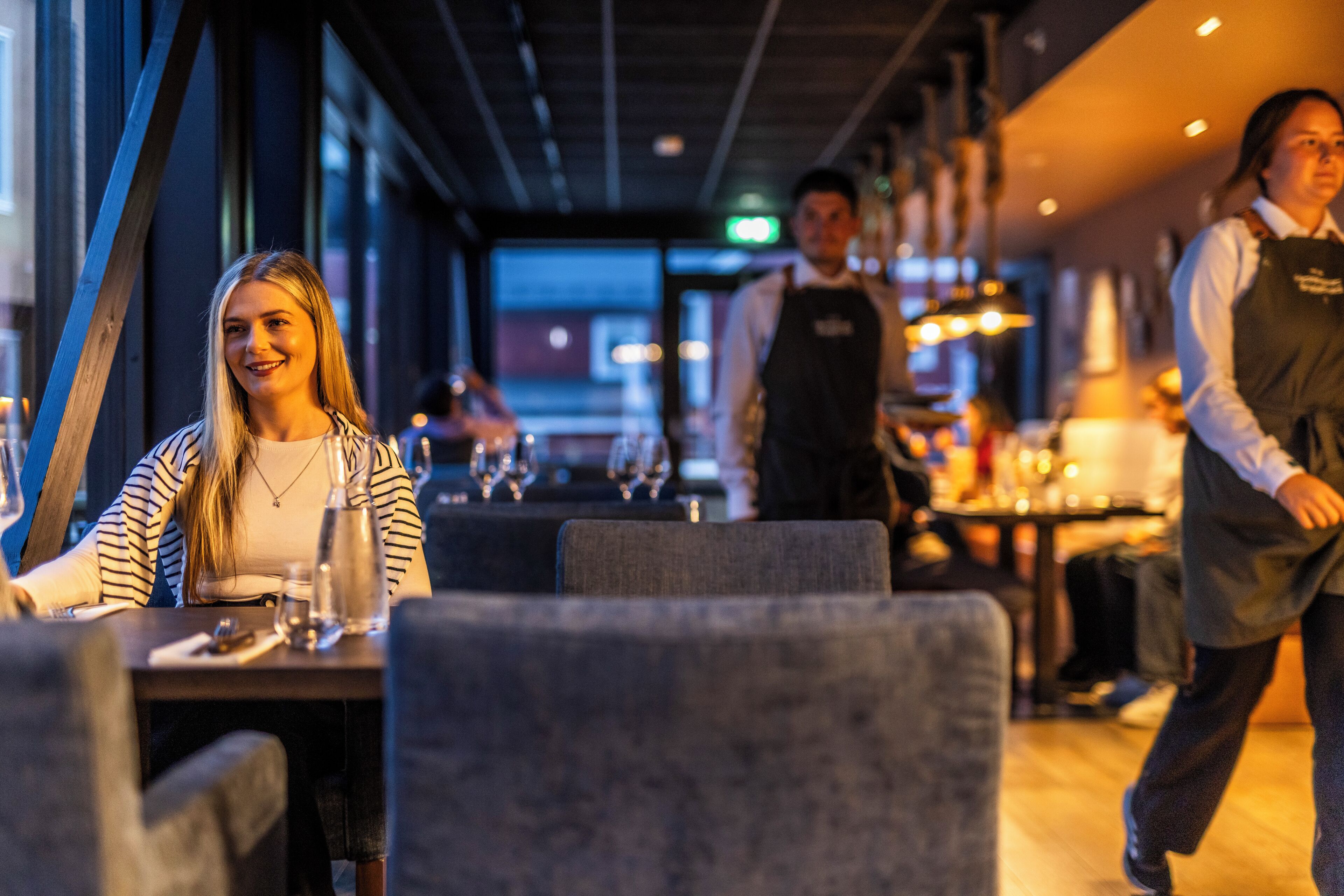 A restaurant interior with tables and chairs, a bar area, and a person walking in the background.