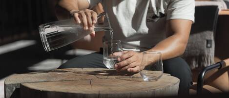 A person pouring water from a clear glass pitcher into a glass on a wooden table.