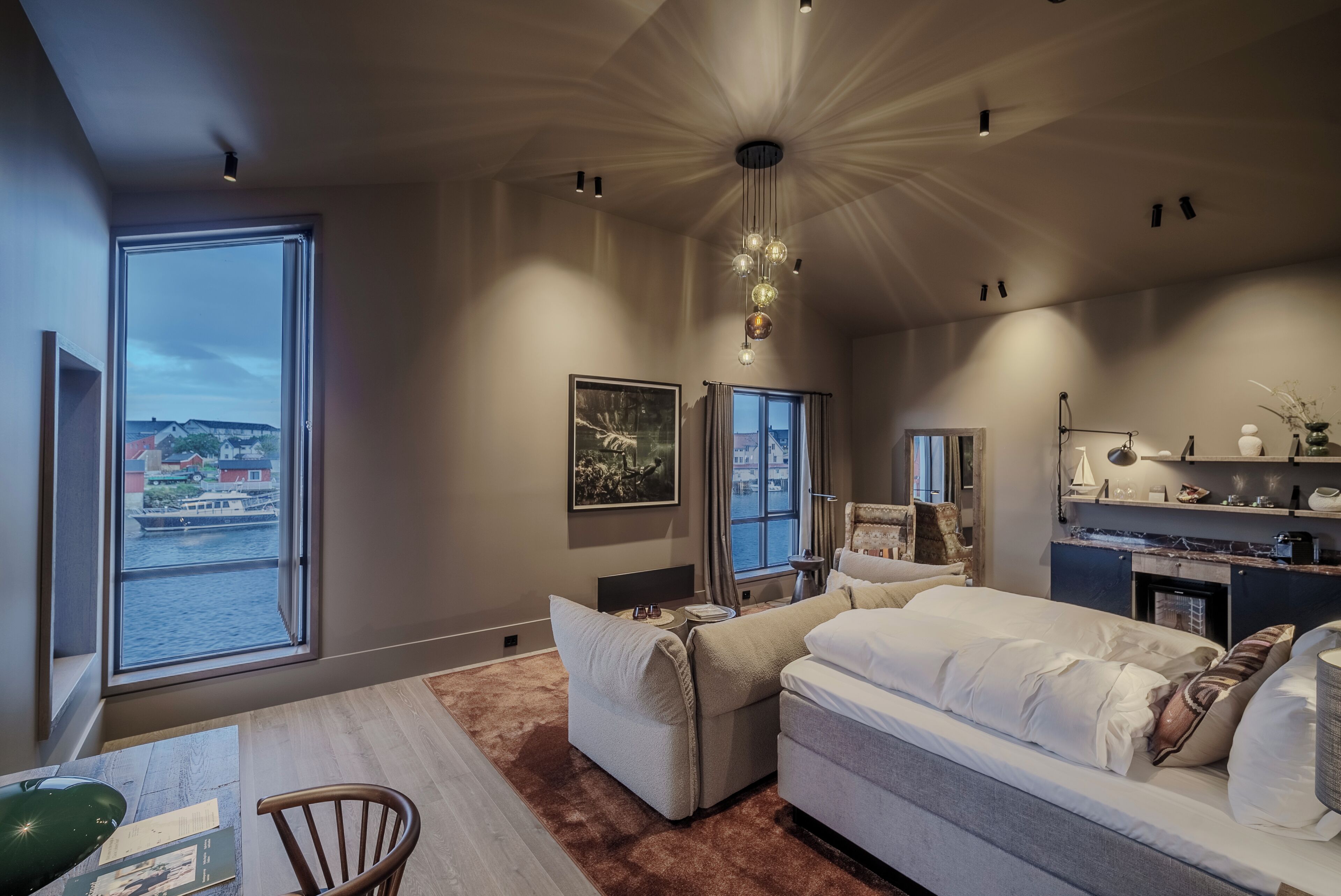 Un dormitorio moderno con un ventanal grande, un sofá, una cama y una zona de escritorio.