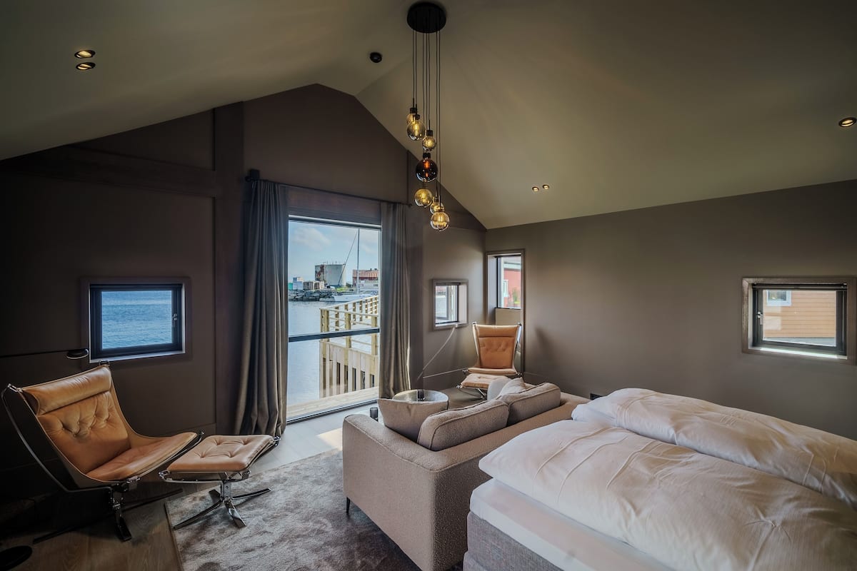 Une chambre d’hôtel moderne, dotée d’un grand lit, d’un canapé, d’un fauteuil et offrant une vue sur la ville.