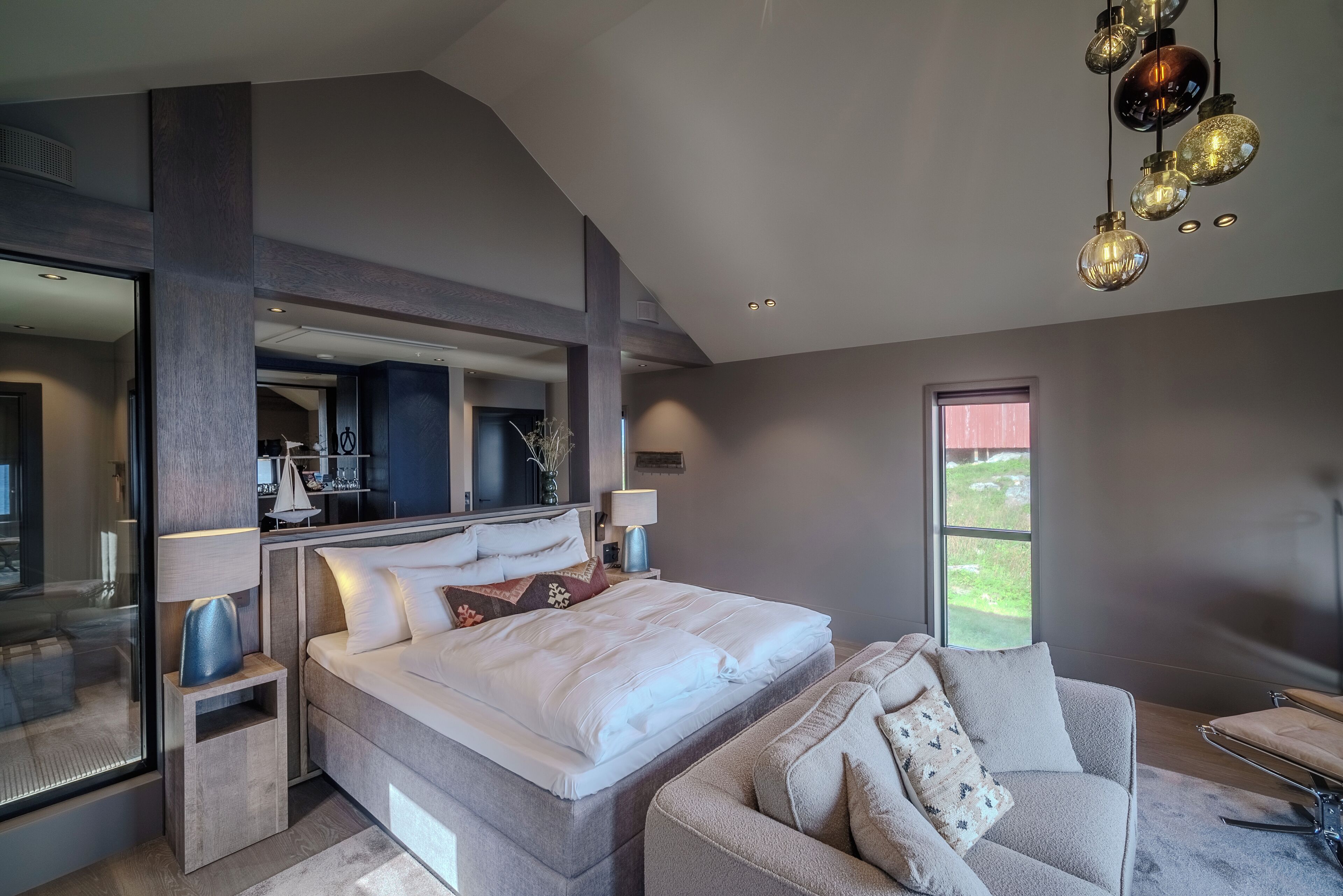A modern bedroom with a large bed, a sofa, and a view of the outdoors.