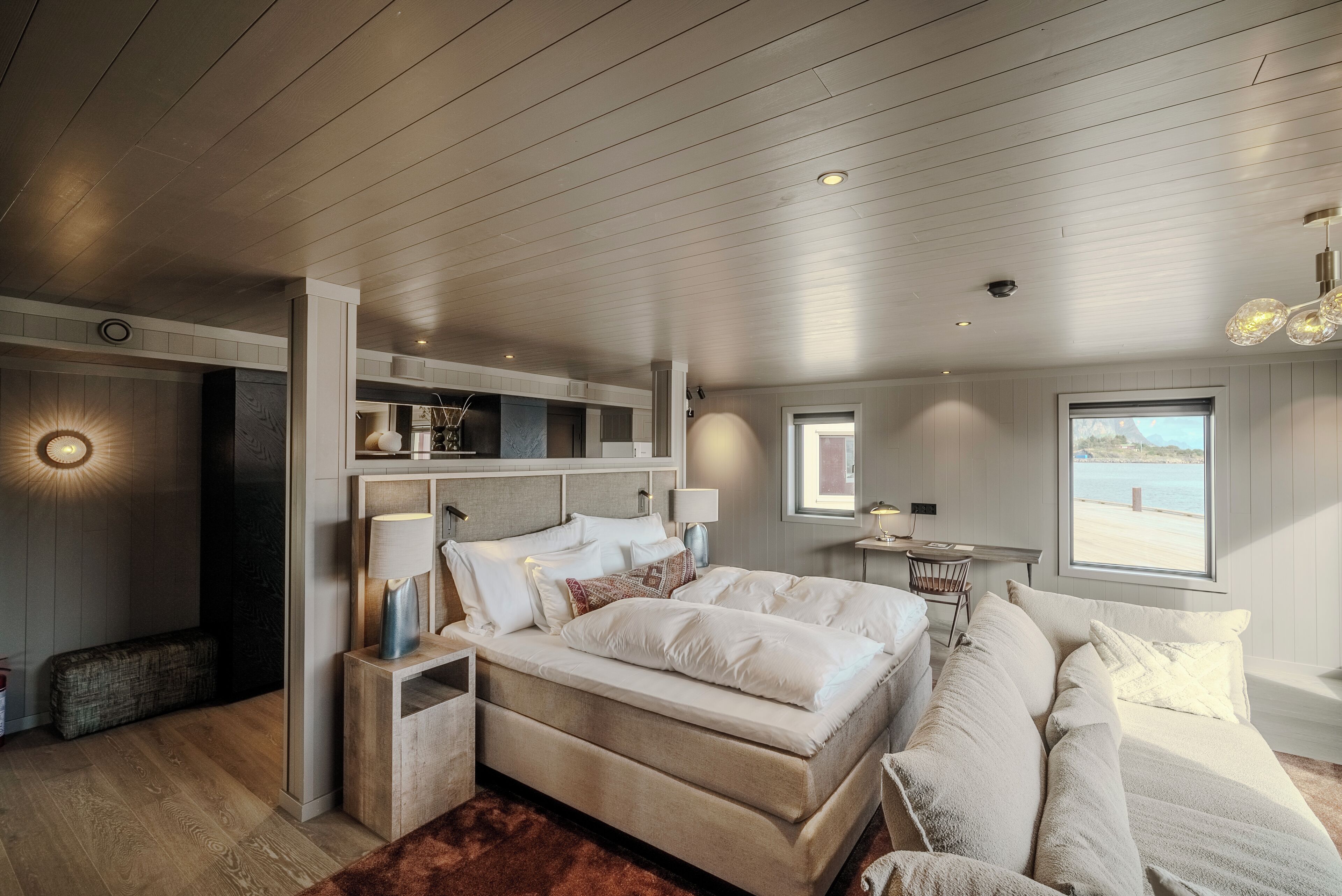A bedroom with a large bed, bedside tables, a nightstand, a sofa, a window with a view, and a built-in shelf.