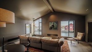 A modern living room with a high ceiling, large windows, a sofa set, a dining table, and a chair. - Henningsvær Bryggehotell - by Classic Norway Hotels (Vagan)