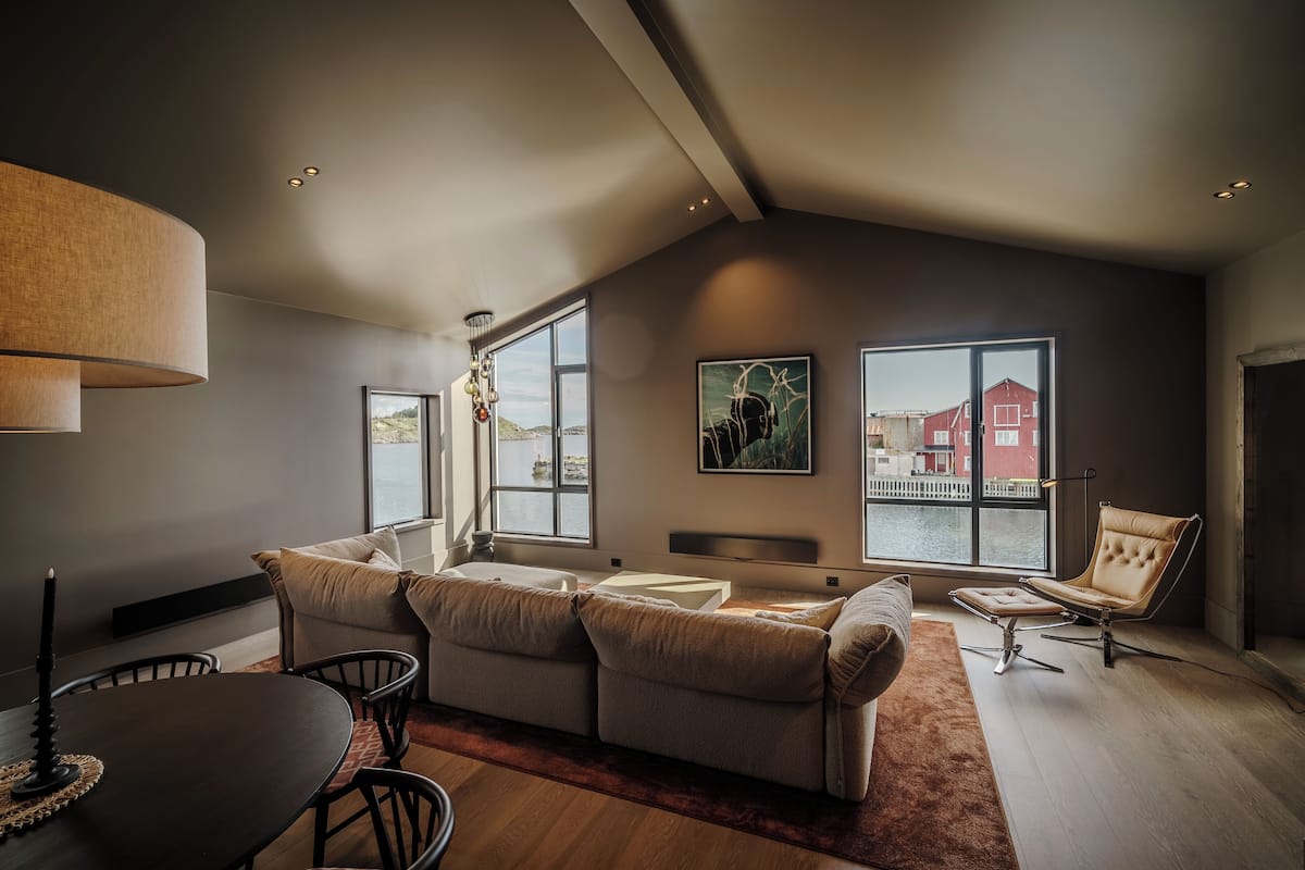 Un salon moderne doté d’un haut plafond, de grandes fenêtres, d’un ensemble de canapés, d’une table à manger et d’une chaise.