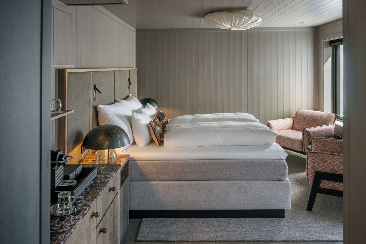 A bedroom with a bed, a chair, a desk with a lamp, and a wardrobe.