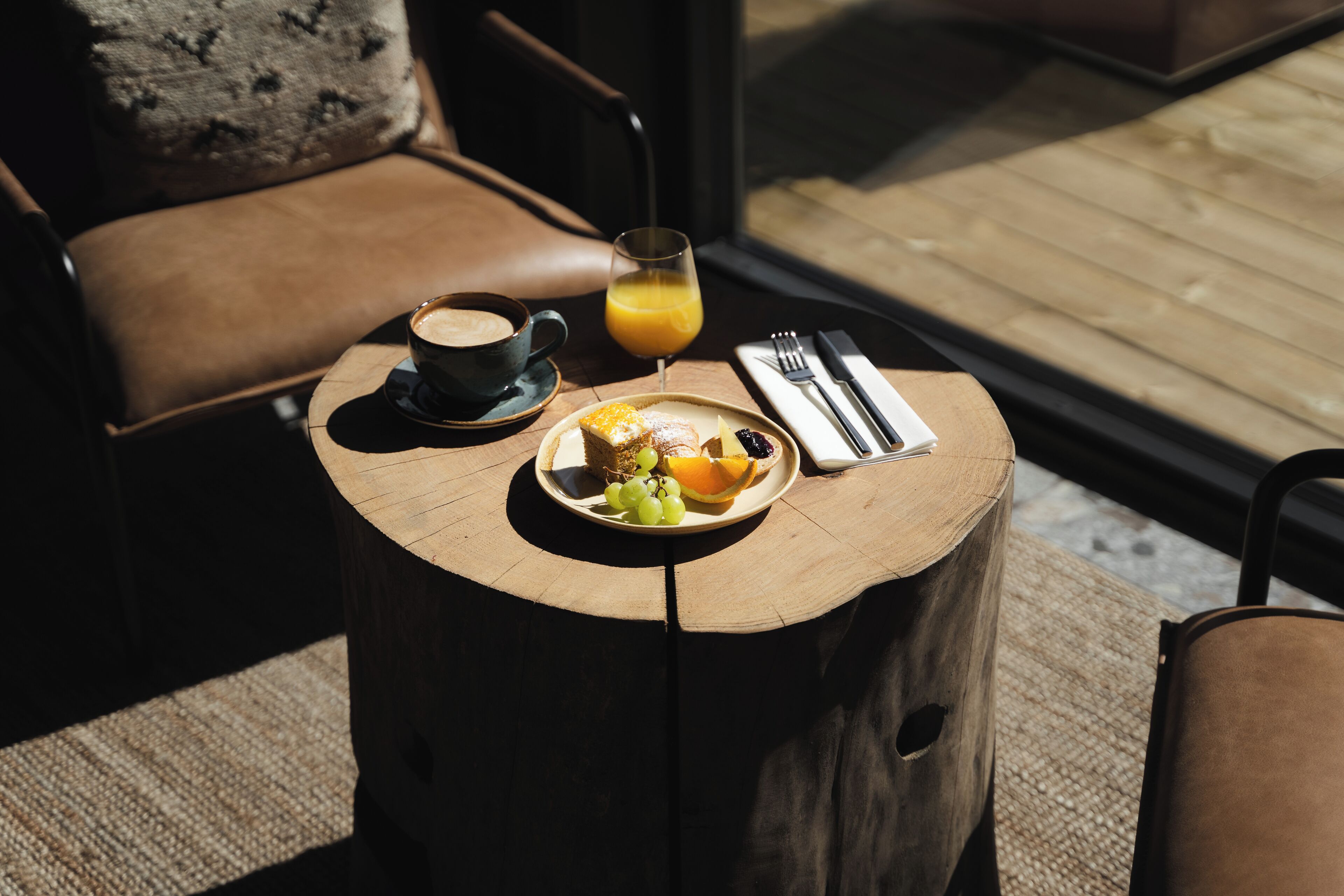 Una mesa de madera redonda con un plato de fruta, una taza de café y un vaso de jugo de naranja.
