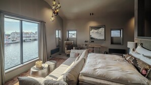 A modern hotel room with a large bed, a sofa, a desk, and a view of a harbor. - Henningsvær Bryggehotell - by Classic Norway Hotels (Vagan)