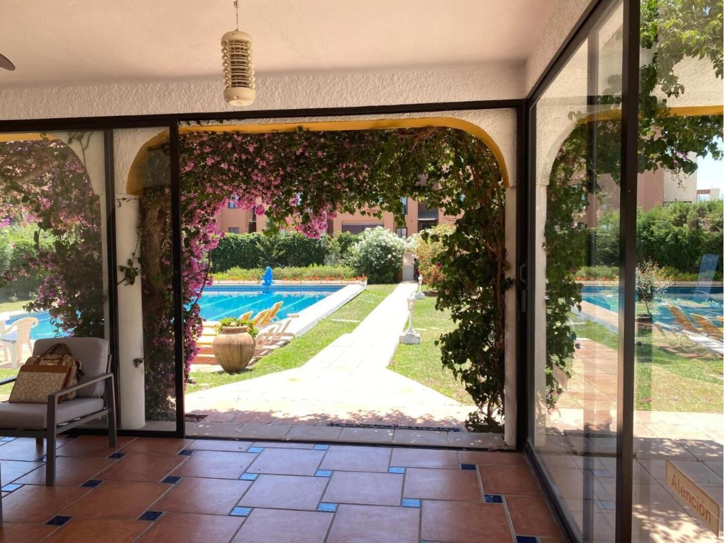 A room with a glass door leading to a pool area, a chair, and a potted plant.