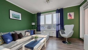 Un salón con sofá, una silla a rayas, una mesa de centro y un ventanal con cortinas.