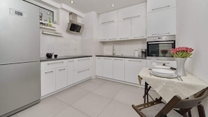 Una cocina moderna con armarios blancos, horno empotrado y comedor con mesa para dos.
