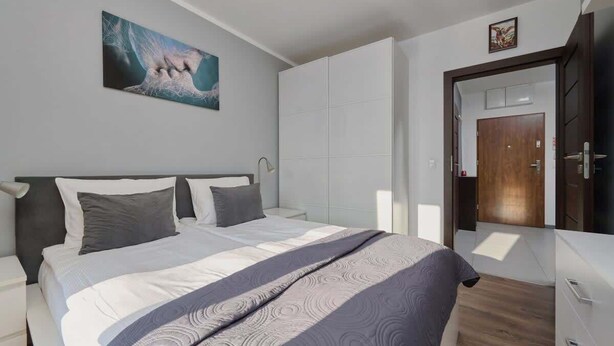 Un dormitorio moderno con cama, armario, mesita de noche y un cuadro en la pared.