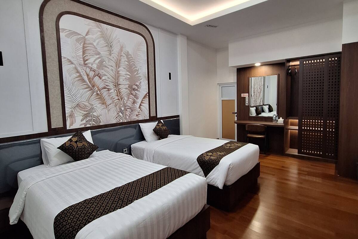 A hotel room with two beds, a desk, a mirror, and a decorative wall piece.