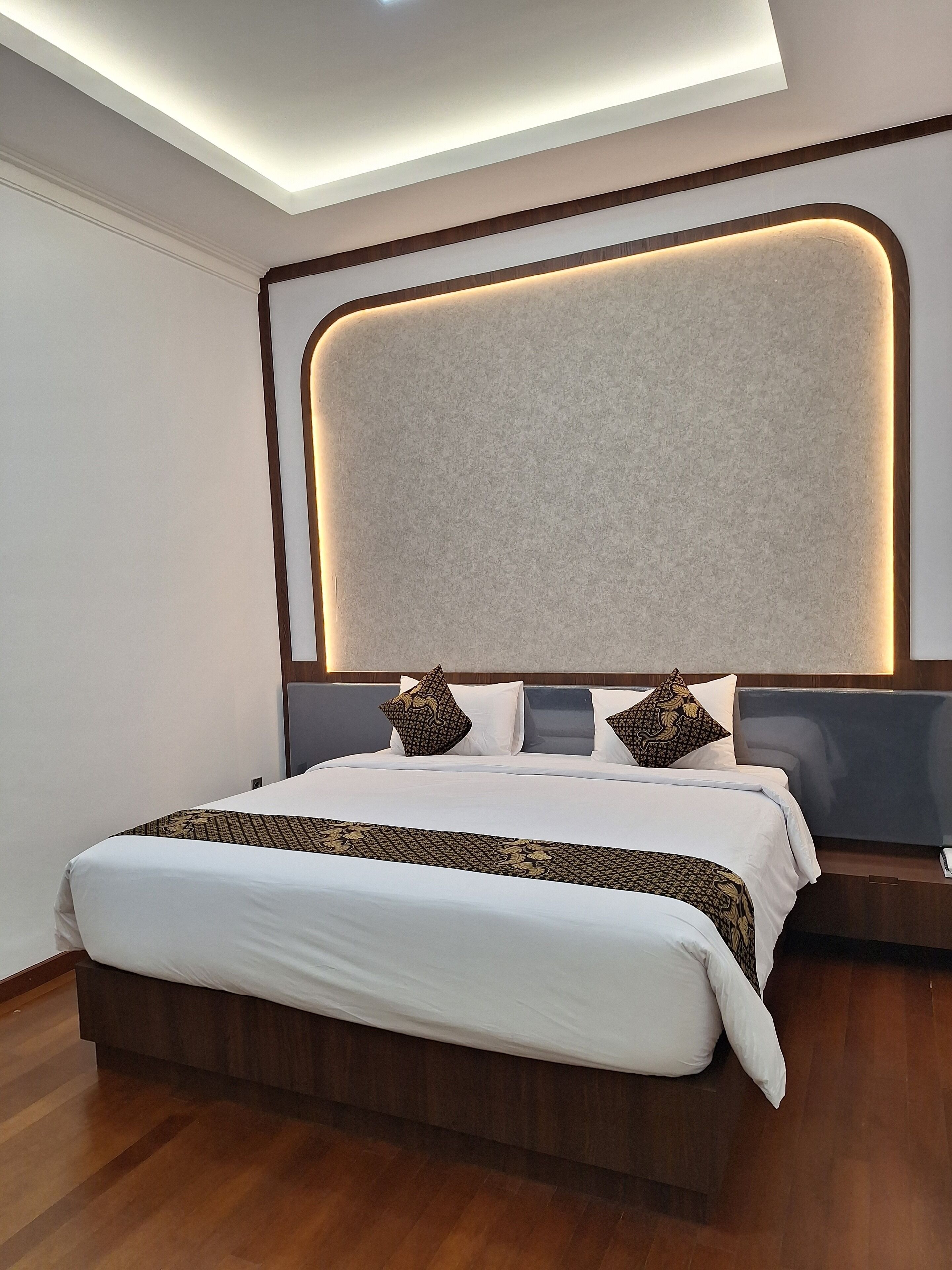 A modern hotel room with a large bed, a wooden headboard, and a ceiling light fixture.