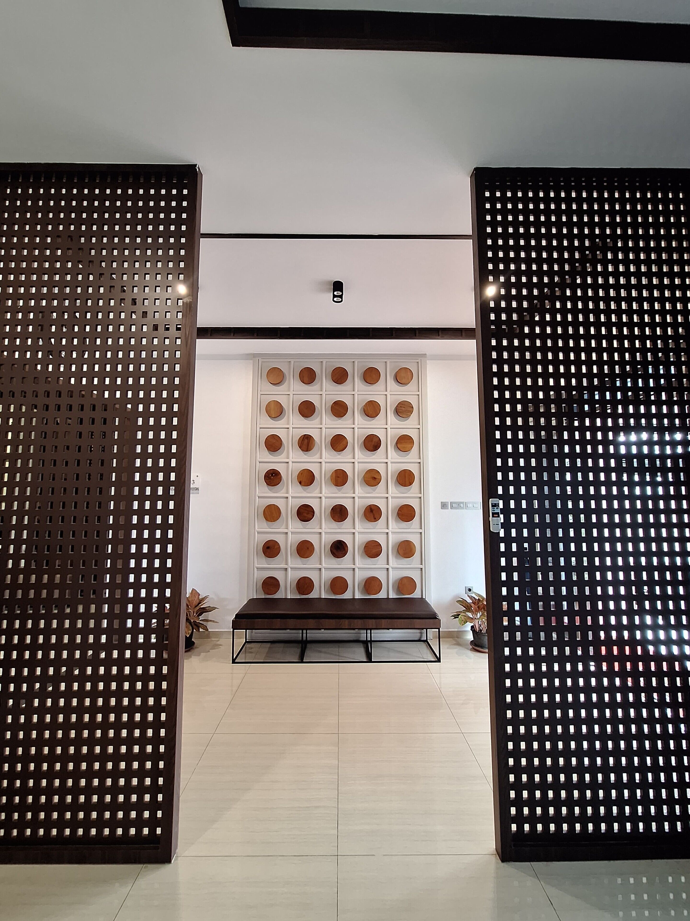 A room with a wooden bench, a wall with circular wooden panels, and a black perforated partition.