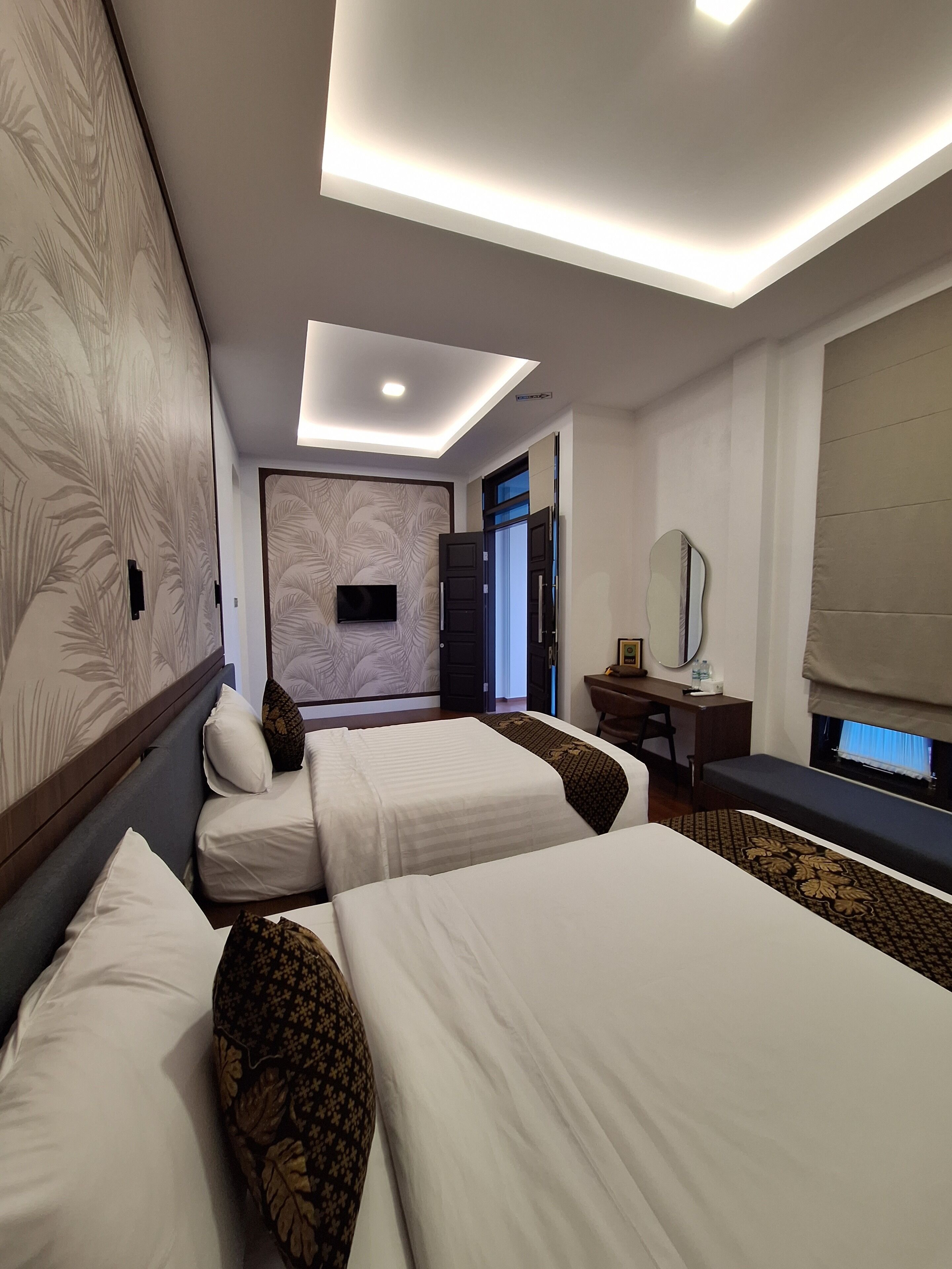 A hotel room with two beds, a desk, a mirror, and a TV.
