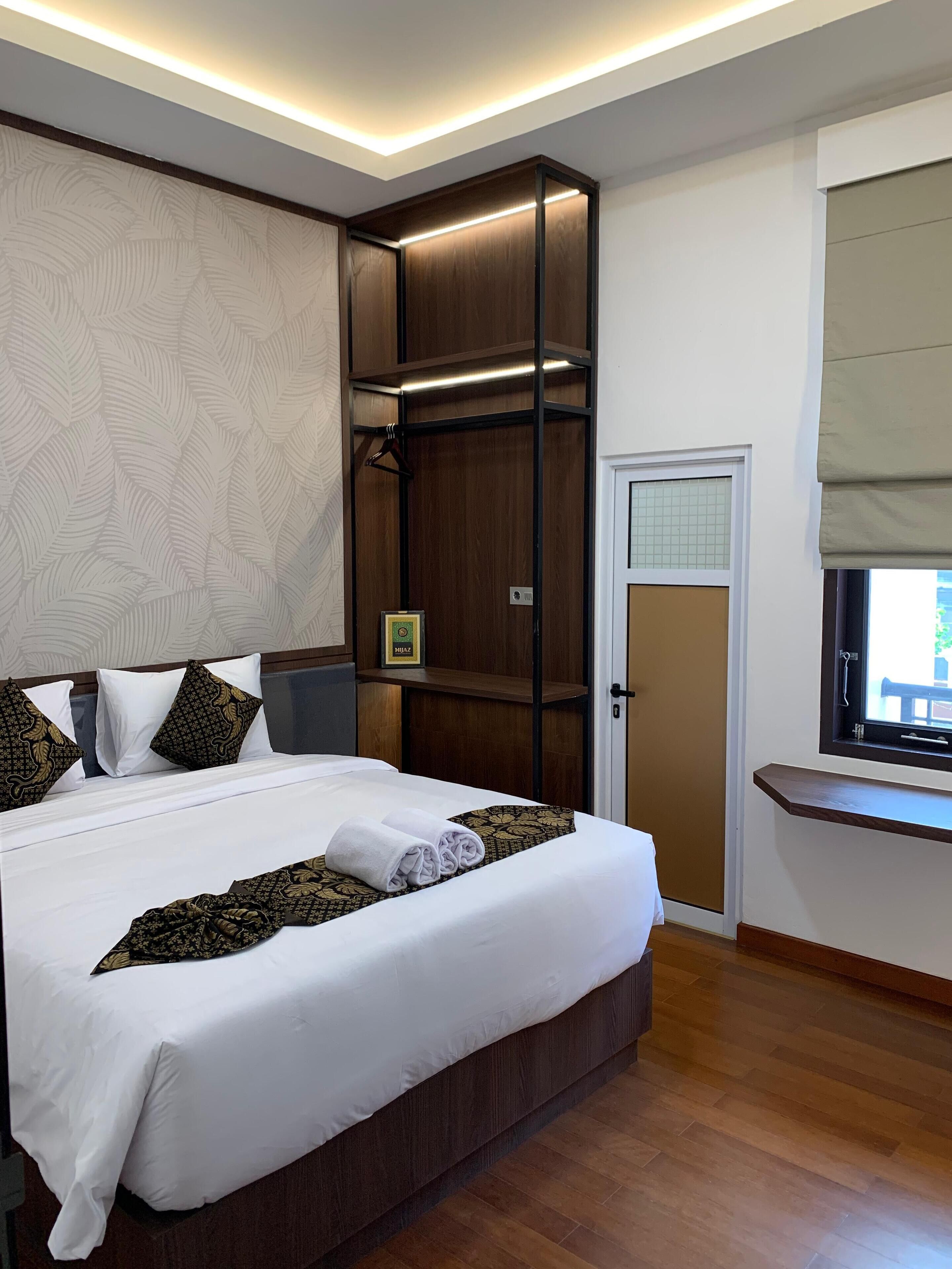 A neatly made bed with white linens and decorative pillows, a wooden headboard, and a built-in wardrobe with a hanging rack.