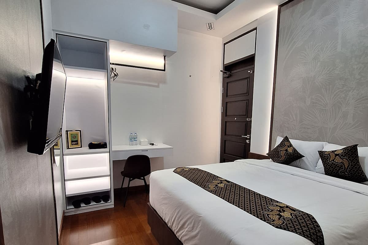 A modern hotel room with a bed, a desk, and a wardrobe.