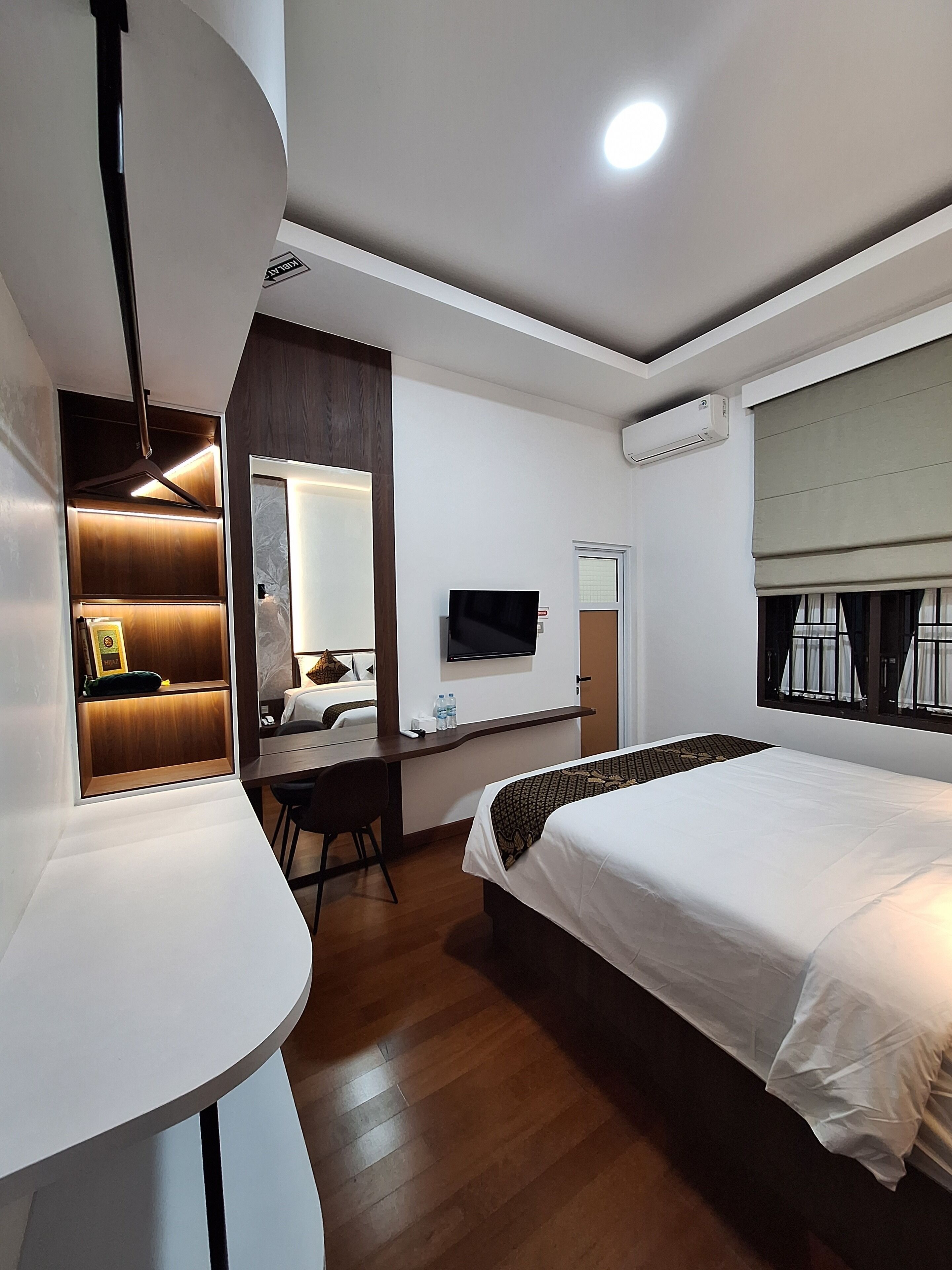A hotel room with a bed, a desk, a chair, a TV, and an air conditioning unit.