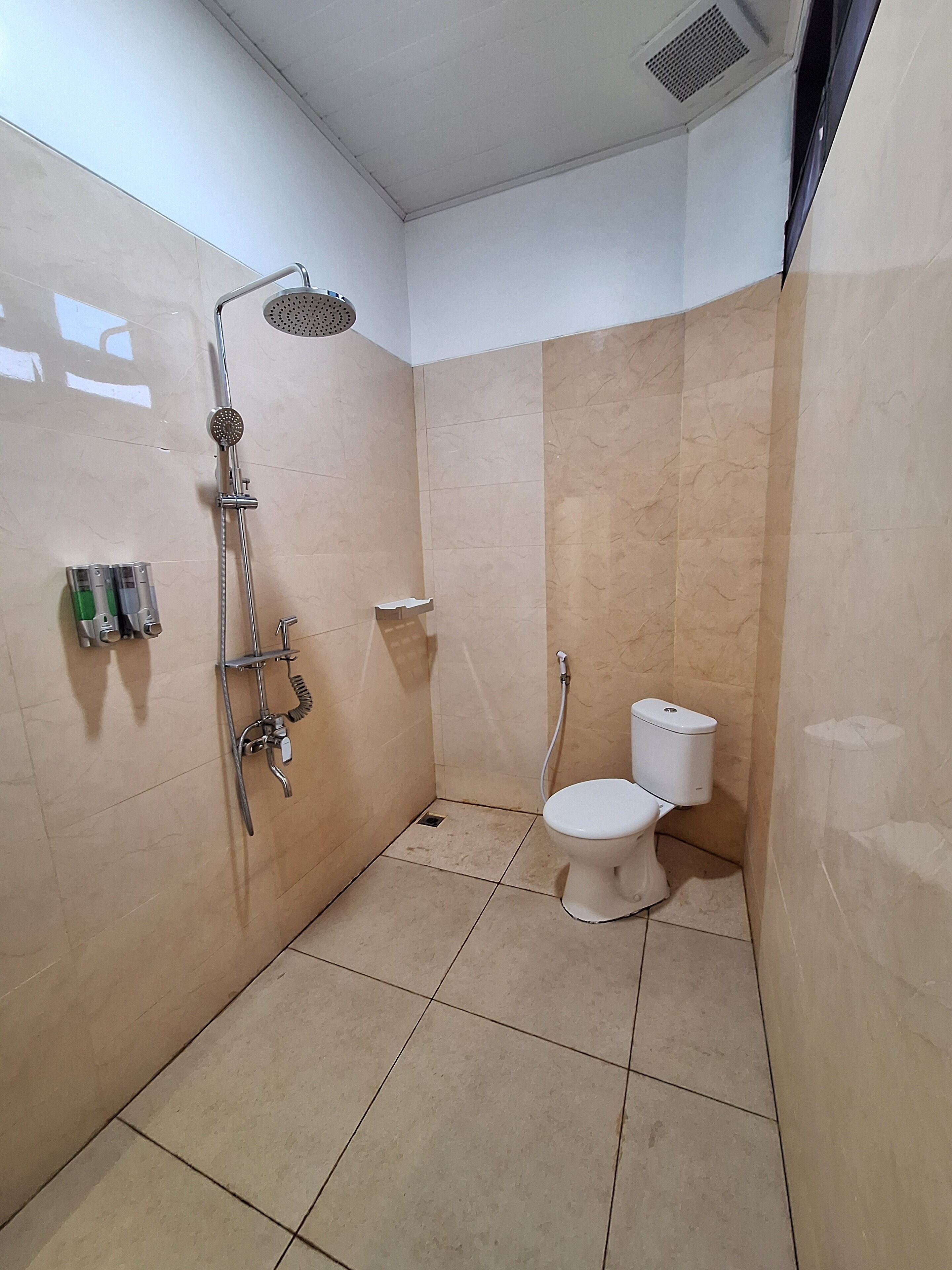 Un baño pequeño con azulejos, ducha, inodoro y repisas con artículos de aseo.