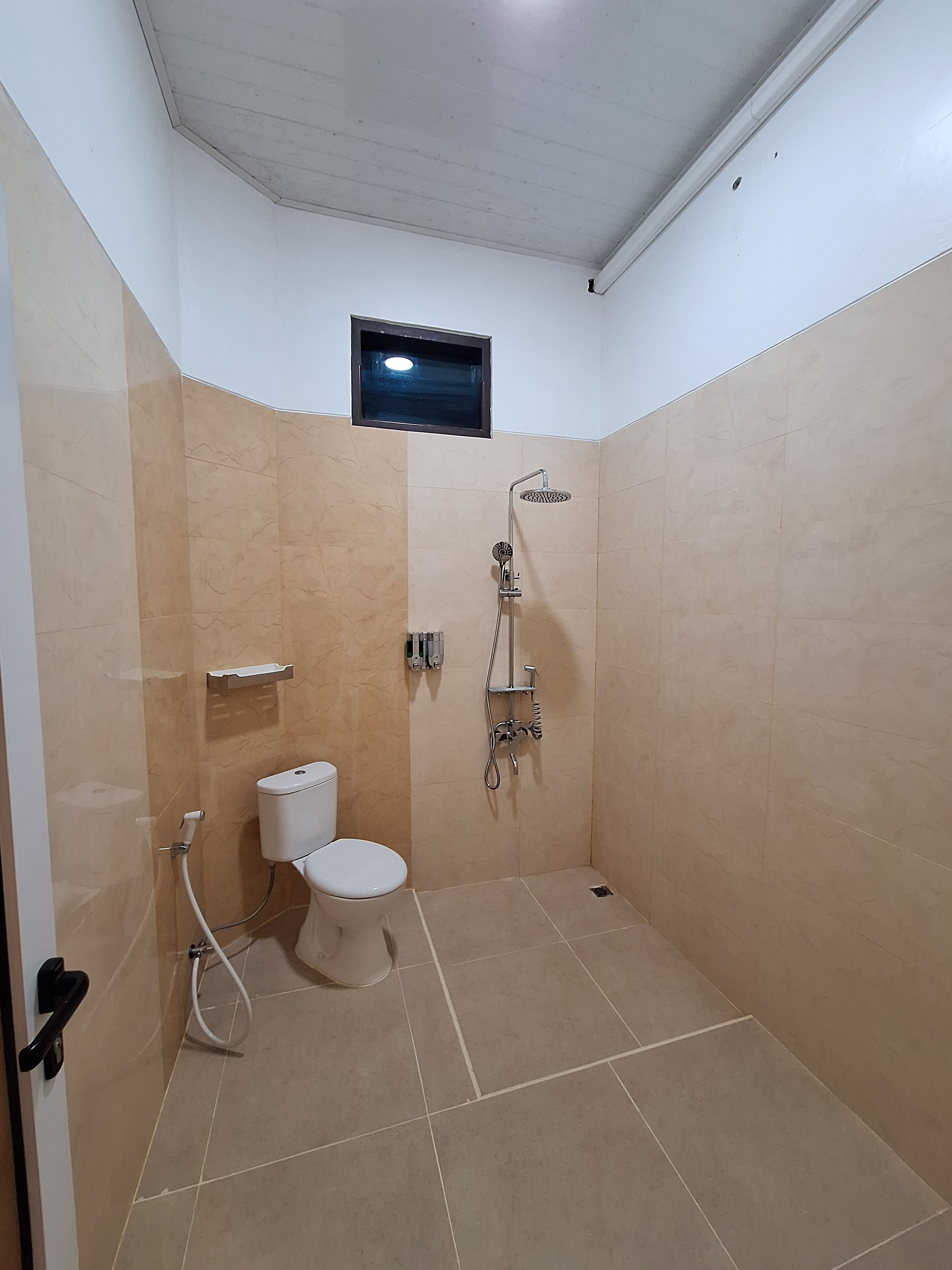 A small, tiled bathroom with a toilet, a shower, and a small window.