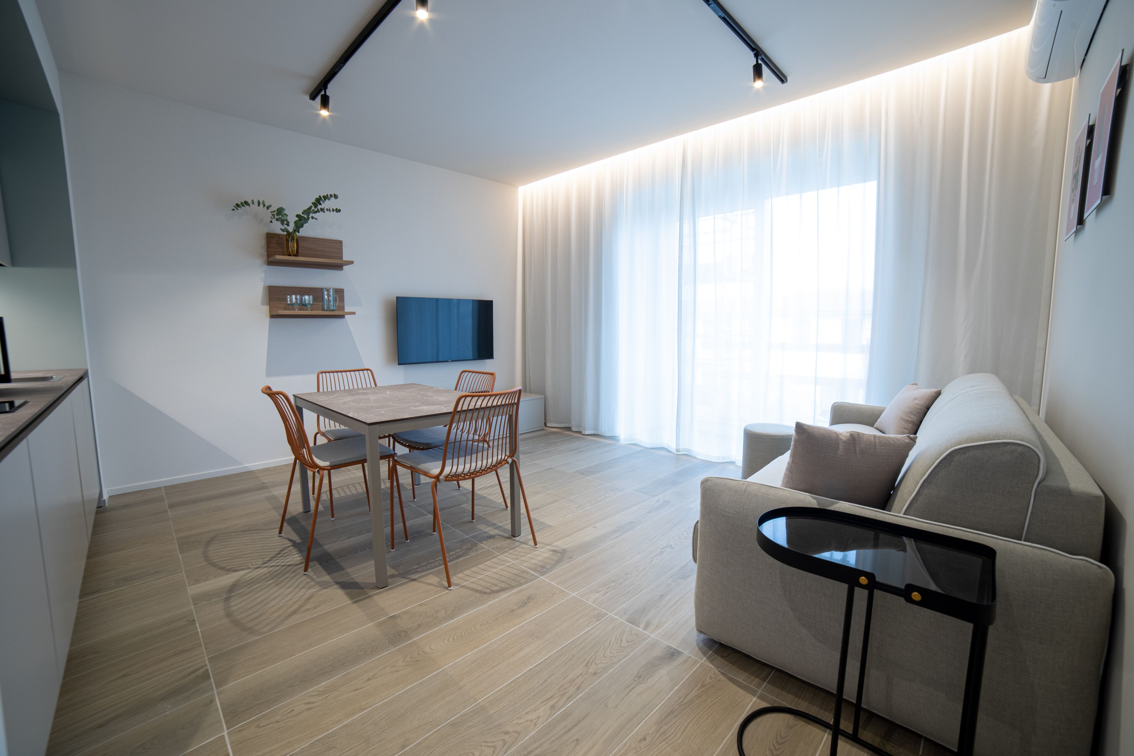 Uma sala de estar moderna com área de jantar, sofá, televisão e cozinha ao fundo.