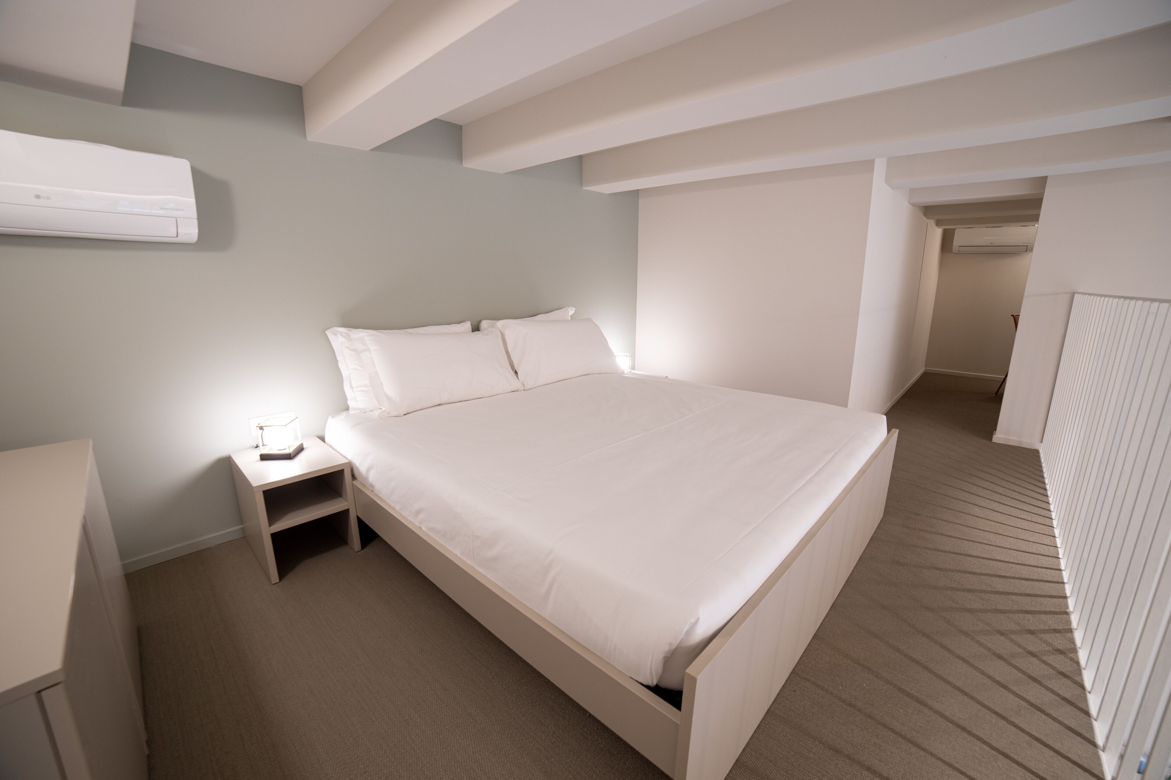 Une chambre avec un grand lit, une table de chevet et un appareil de climatisation fixé au mur.