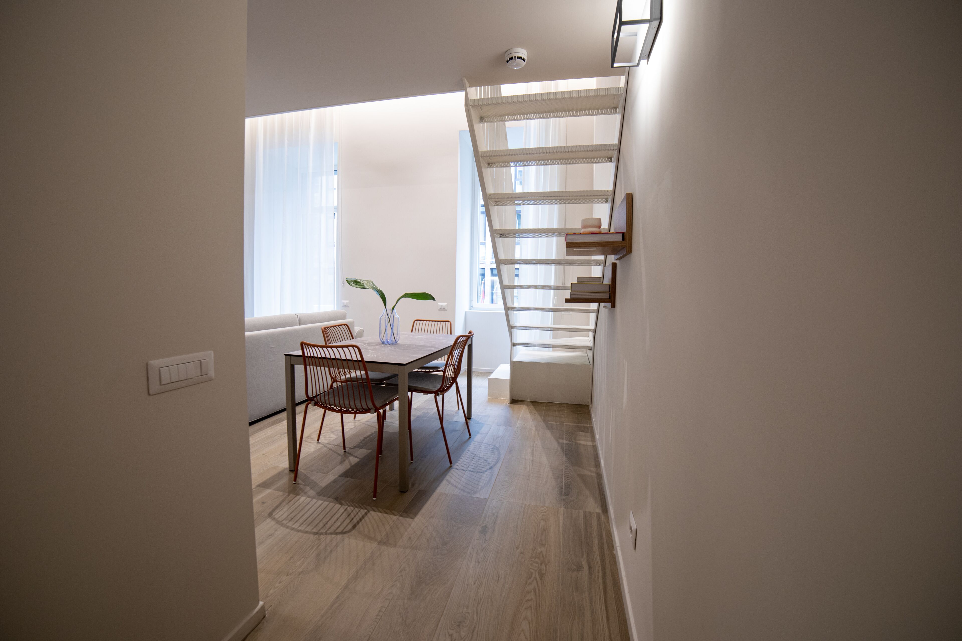 A modern dining area with a wooden table and chairs, a small plant, and a staircase with a white railing.