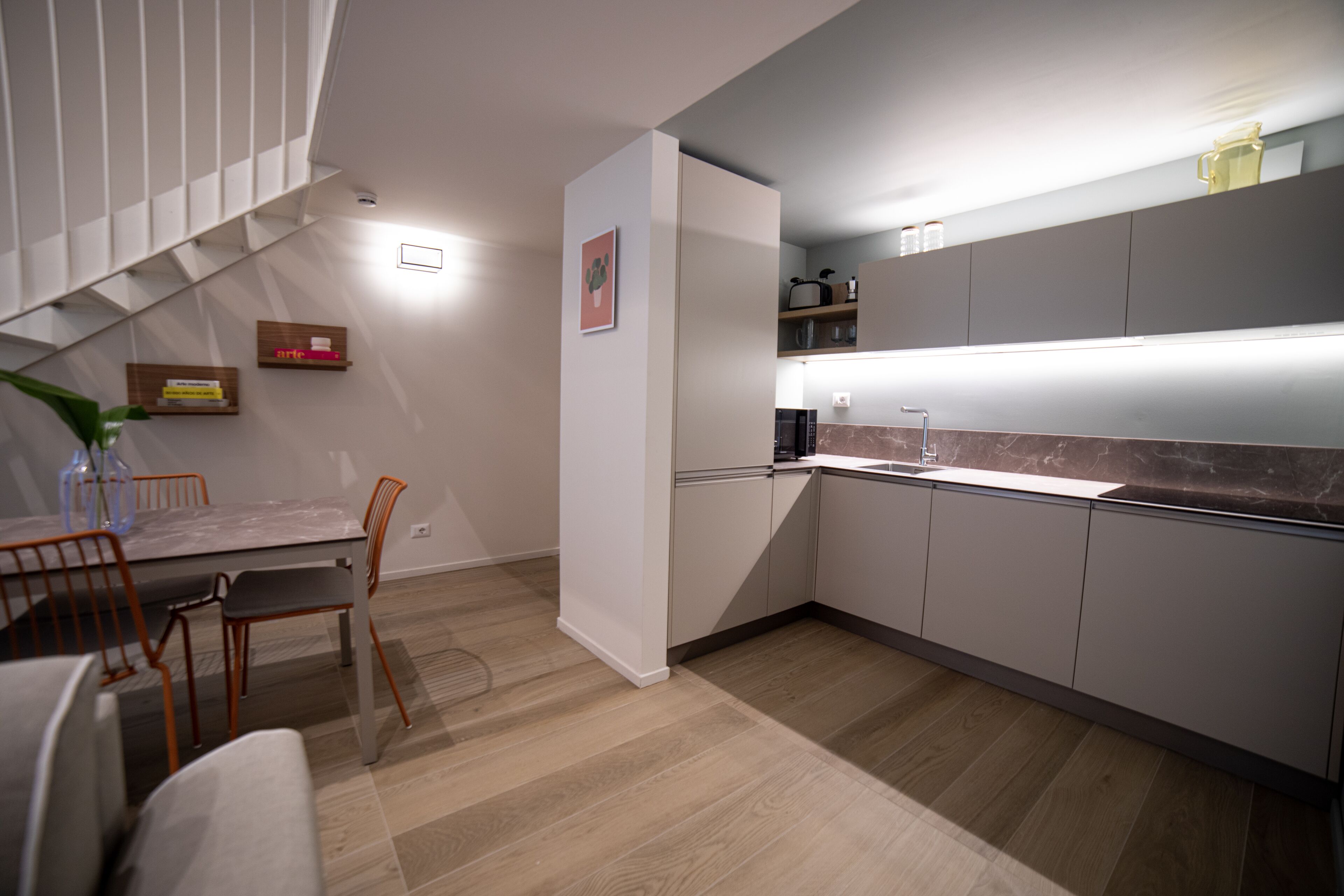 A modern kitchen with grey cabinets, a marble countertop, and a dining area with a table and chairs.