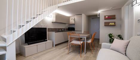 Ein modernes Apartment mit einer Treppe zu einem Schlafboden, einem Essbereich mit Tisch und Stühlen, einem Sofa und einem Fernseher im Wohnzimmer.
