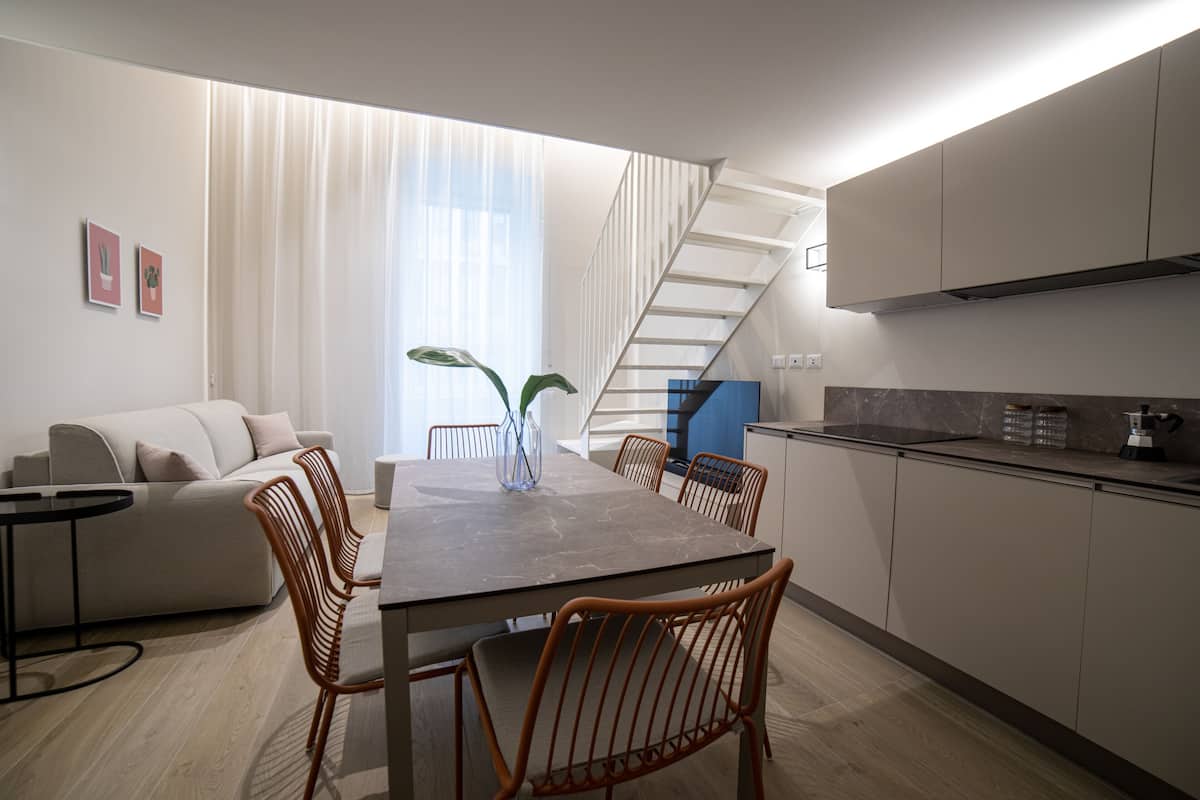 A modern kitchen with a dining area, featuring a staircase, a sofa, and a coffee table.