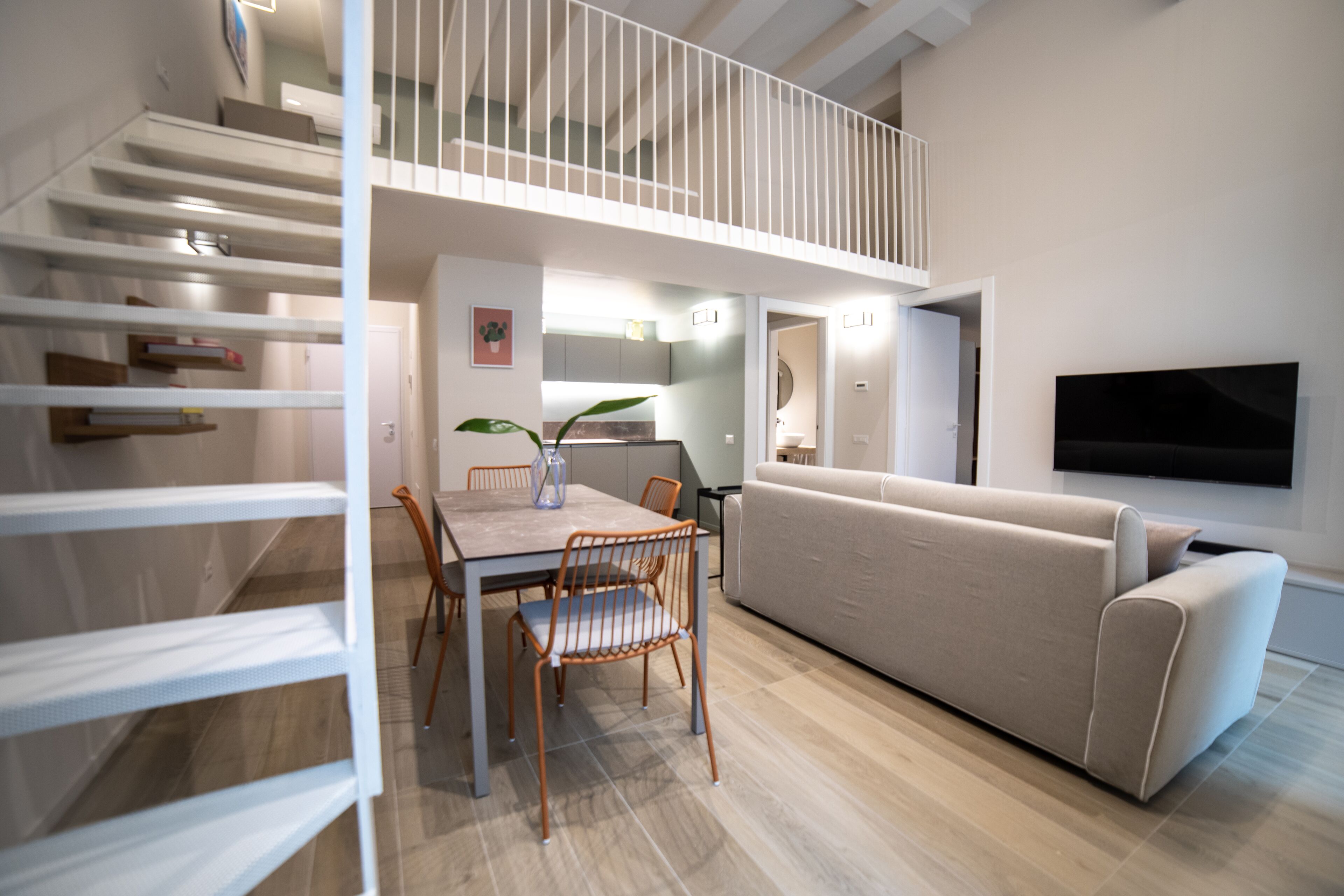 A modern living room with a sofa, a dining table with chairs, and a staircase leading to an upper level.