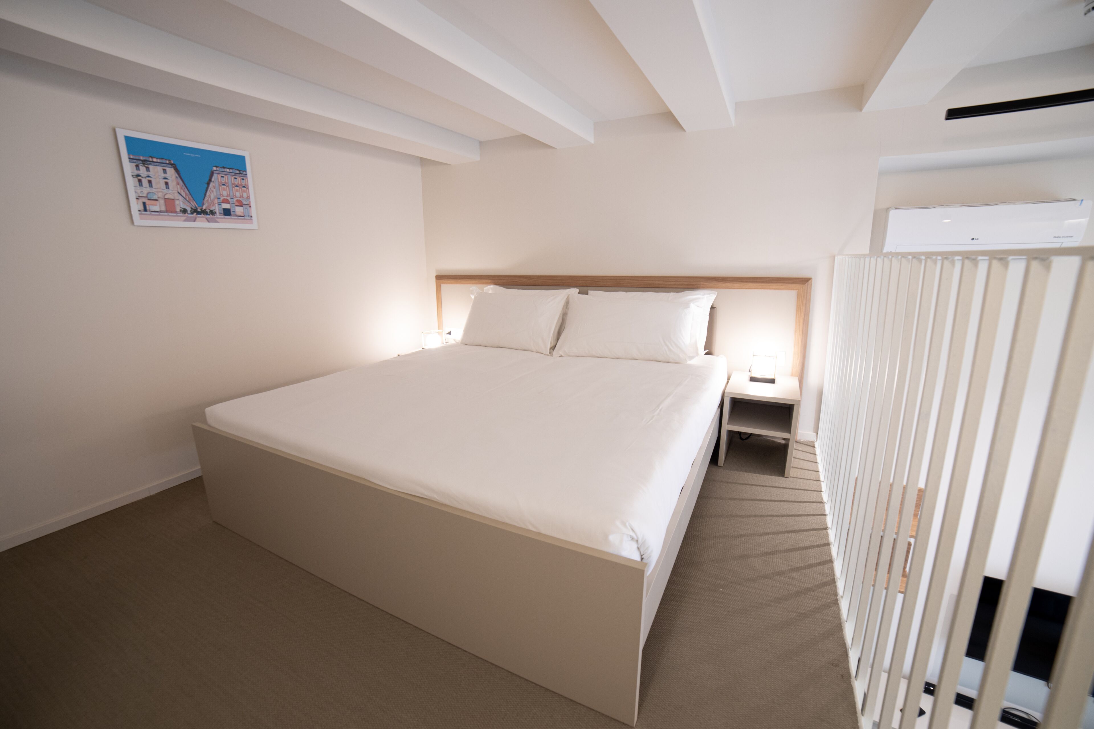 A hotel room with a large bed, a nightstand, a wall-mounted air conditioner, and a framed picture on the wall.