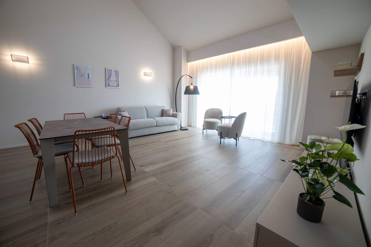 A modern living room with a dining area, a sofa, and a coffee table. There is a potted plant on a side table.