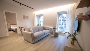 A modern living room with a sofa, a dining table, and a TV mounted on the wall. - Be Mate Torino Centro (Turin)