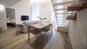 A modern living space with a dining area, a sofa, a TV mounted on the wall, and a staircase leading to an upper level. - Be Mate Torino Centro (Turin)