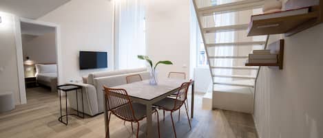 Un espace de vie moderne comprenant un coin repas, un canapé, un téléviseur fixé au mur et un escalier menant à un niveau supérieur.