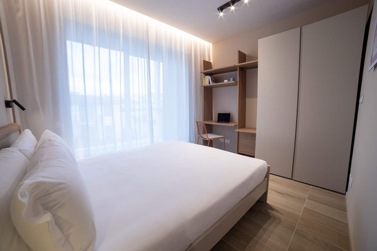A modern bedroom with a large bed, a desk, and a wardrobe.