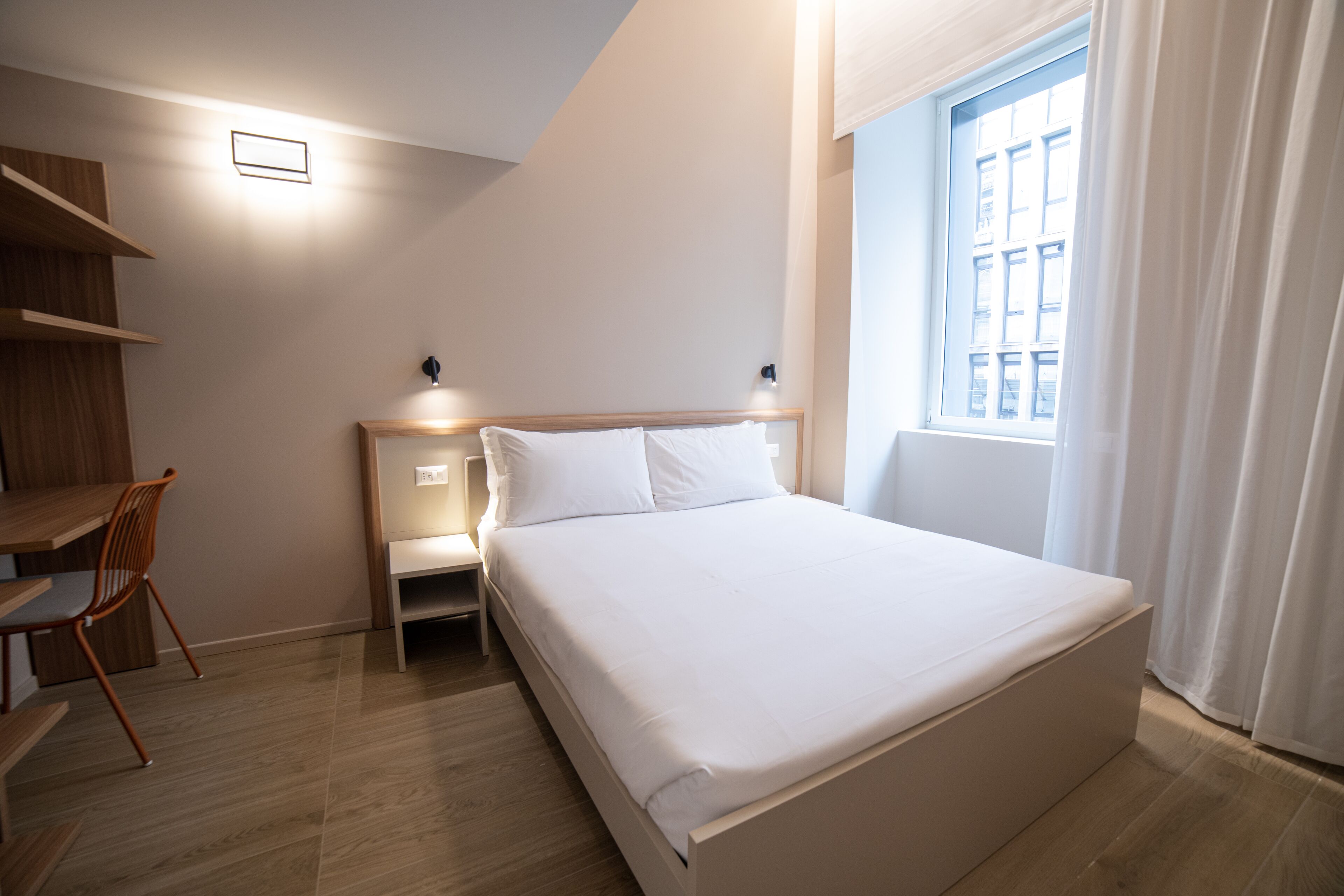 A modern hotel room with a large bed, a desk, and a chair.