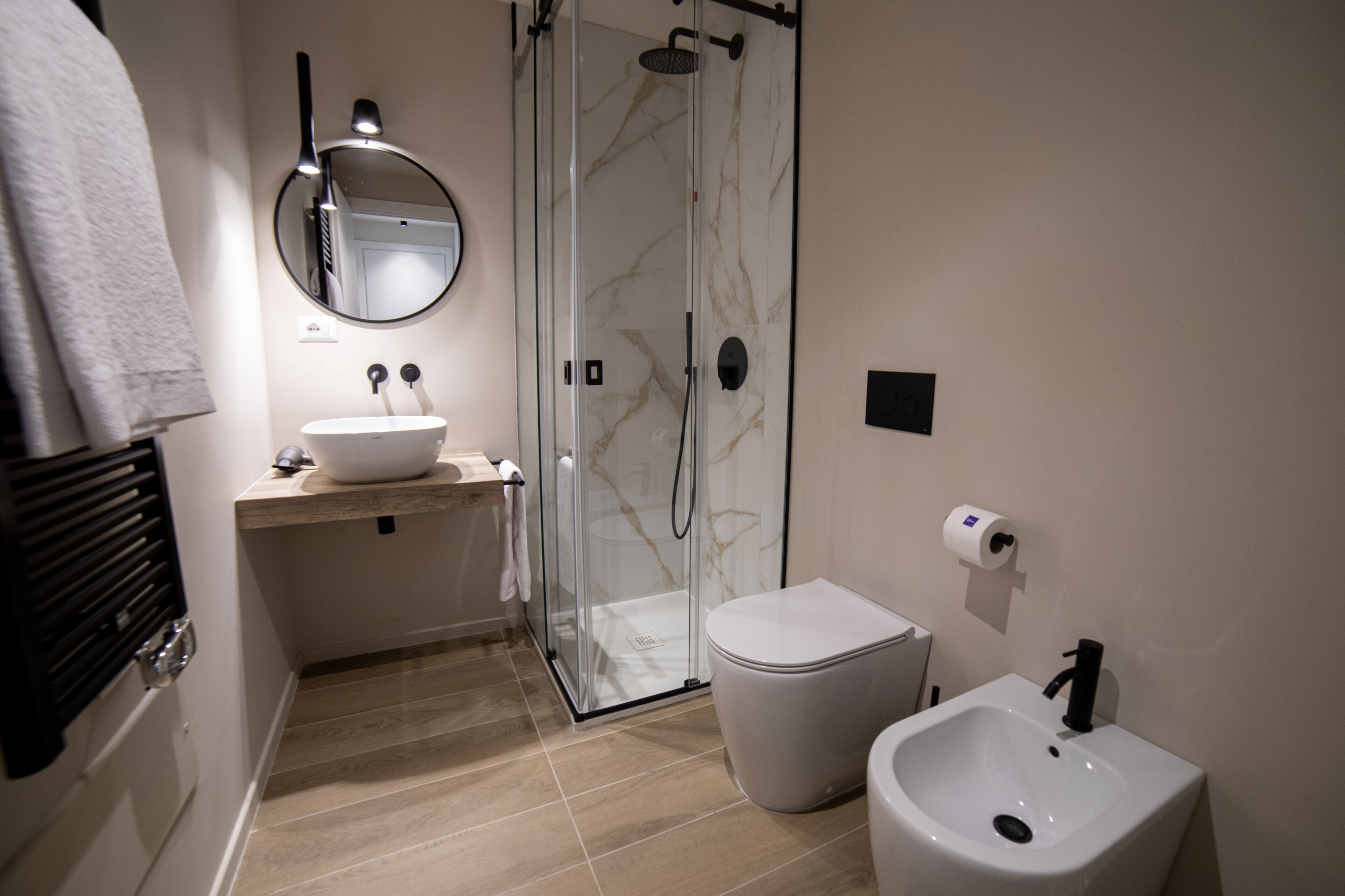 A modern bathroom with a glass-enclosed shower, a white sink, a bidet, and a mirror above the sink.