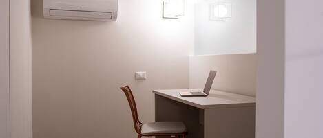 A small, modern room with a desk, chair, and an air conditioning unit mounted on the wall.