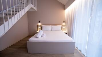 A modern bedroom with a large bed, a staircase, and a view of the city through sheer curtains.