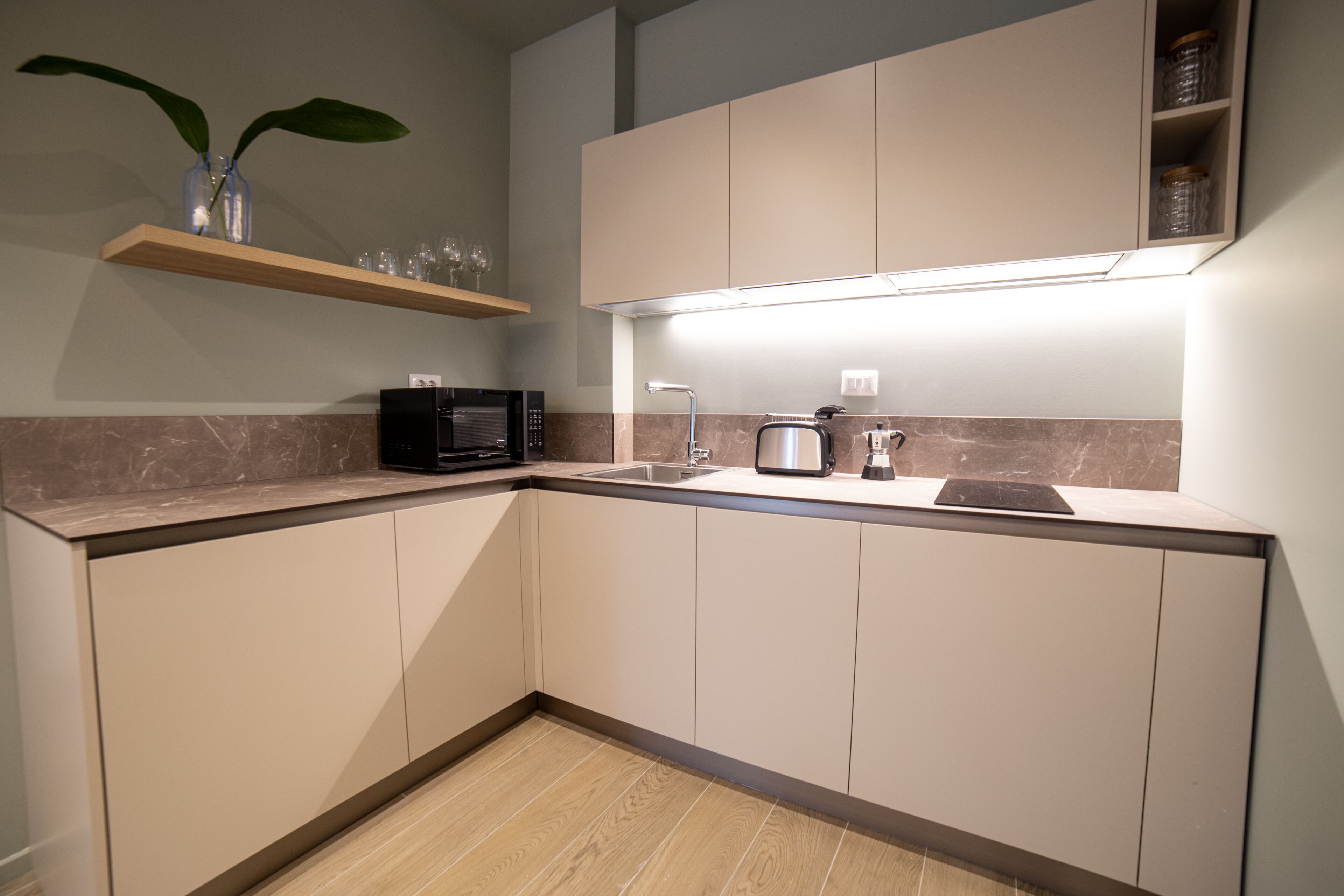 A modern kitchen with a microwave, toaster, and sink. There is a shelf with wine glasses and a plant.