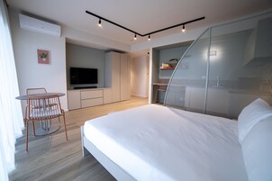 A modern bedroom with a bed, a TV, a small dining area, and a balcony with a mesh screen.
