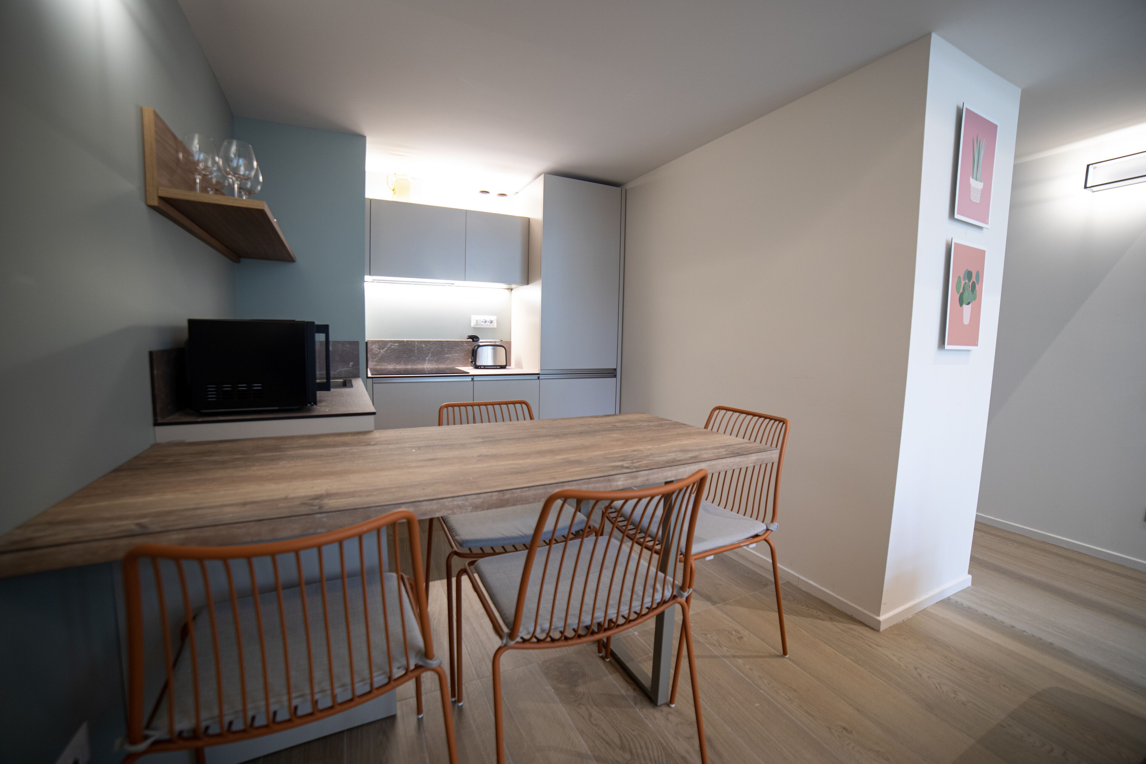 Una cocina moderna con una mesa de madera y cuatro sillas, una cafetera y una estantería con vasos.
