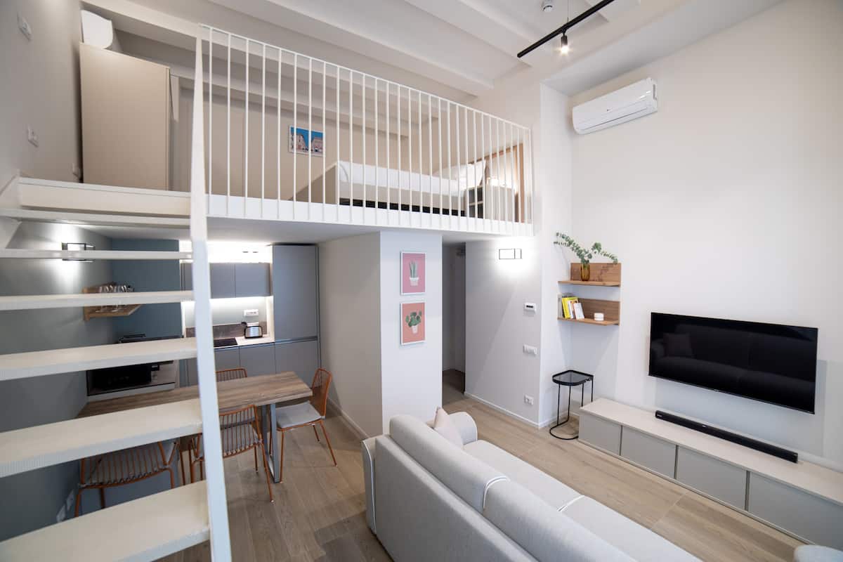 A modern apartment with a loft bedroom, a dining area, and a living room with a flat-screen TV.