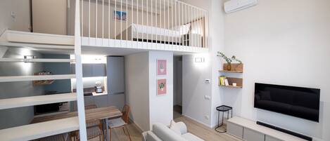 A modern apartment with a loft bedroom, a dining area, and a living room with a flat-screen TV.