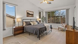 Ein Schlafzimmer mit Bett, Nachttischen, Schreibtisch, Stuhl, Deckenventilator und großen Fenstern.