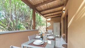 An outdoor dining area with a table set for two, surrounded by chairs, and a bottle of wine on the table. - White Sand House (Olbia)